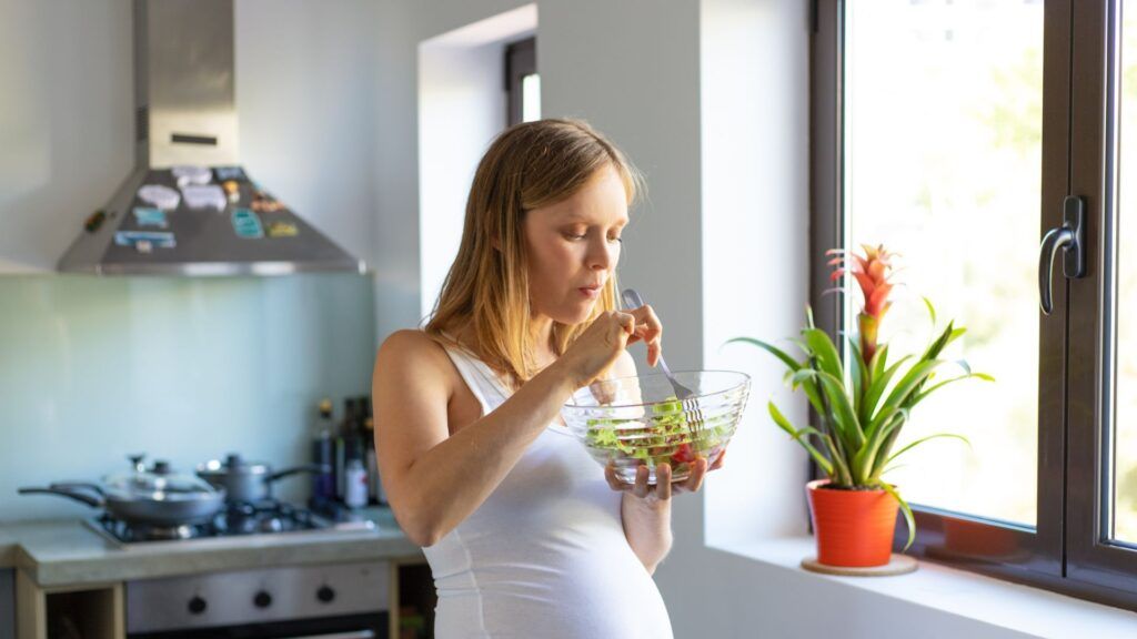 Salud bucodental y embarazo: Mitos, verdades y cuidados esenciales Mujer embarazada comiendo una ensalada saludable en casa, reflejando la importancia de la alimentación en la salud bucodental durante la gestación.
